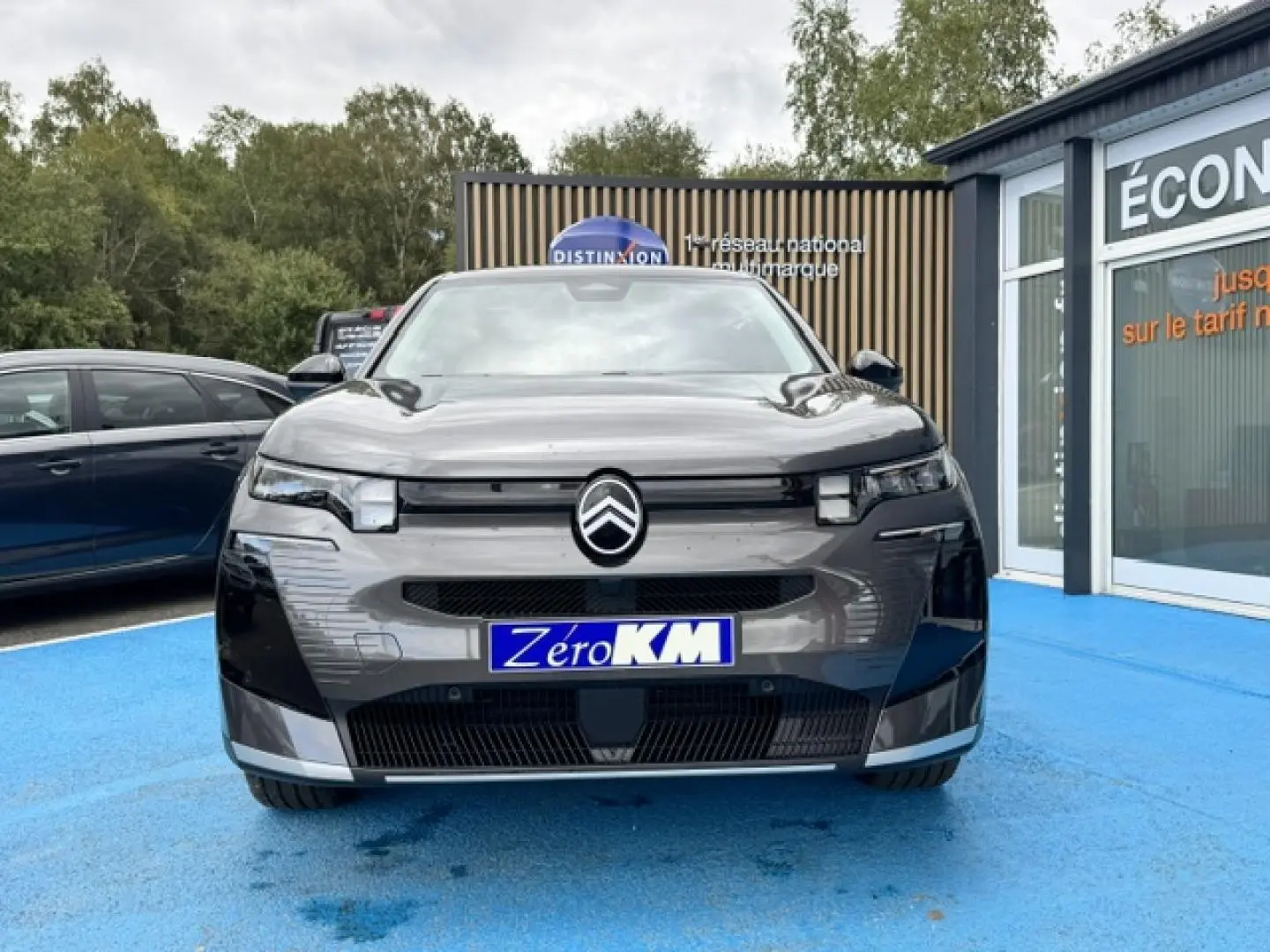 Vue frontale d'un Citroën C5 Aircross gris Platinium avec logo distinctif et plaque "Zéro KM" sur un sol bleu.