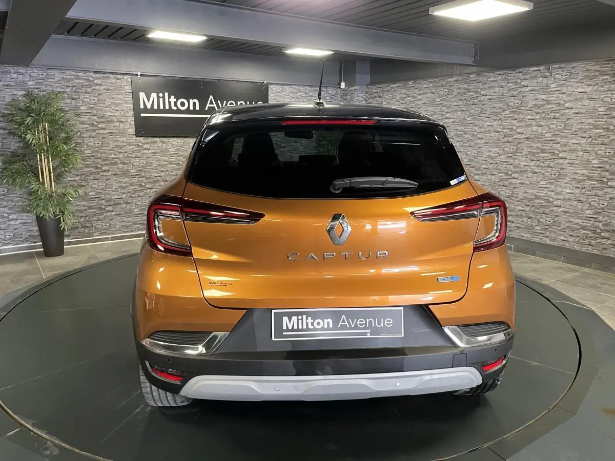 Vue arrière d'un Renault Captur orange avec toit noir, feux LED en forme de C et logo central sur fond intérieur gris.