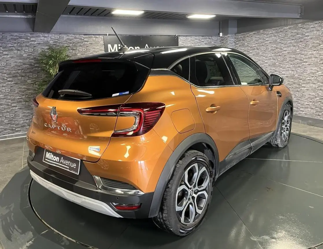 Vue 3/4 arrière droite du Renault Captur 1.6 E-Tech hybride rechargeable orange avec toit noir et jantes alliage 18 pouces.