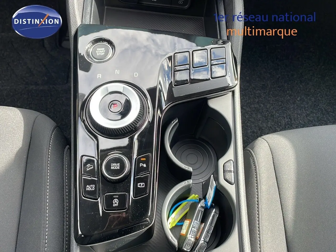 Vue plongeante sur la console centrale noire brillante du Kia Sportage 2025 avec molette de sélection et porte-gobelets.