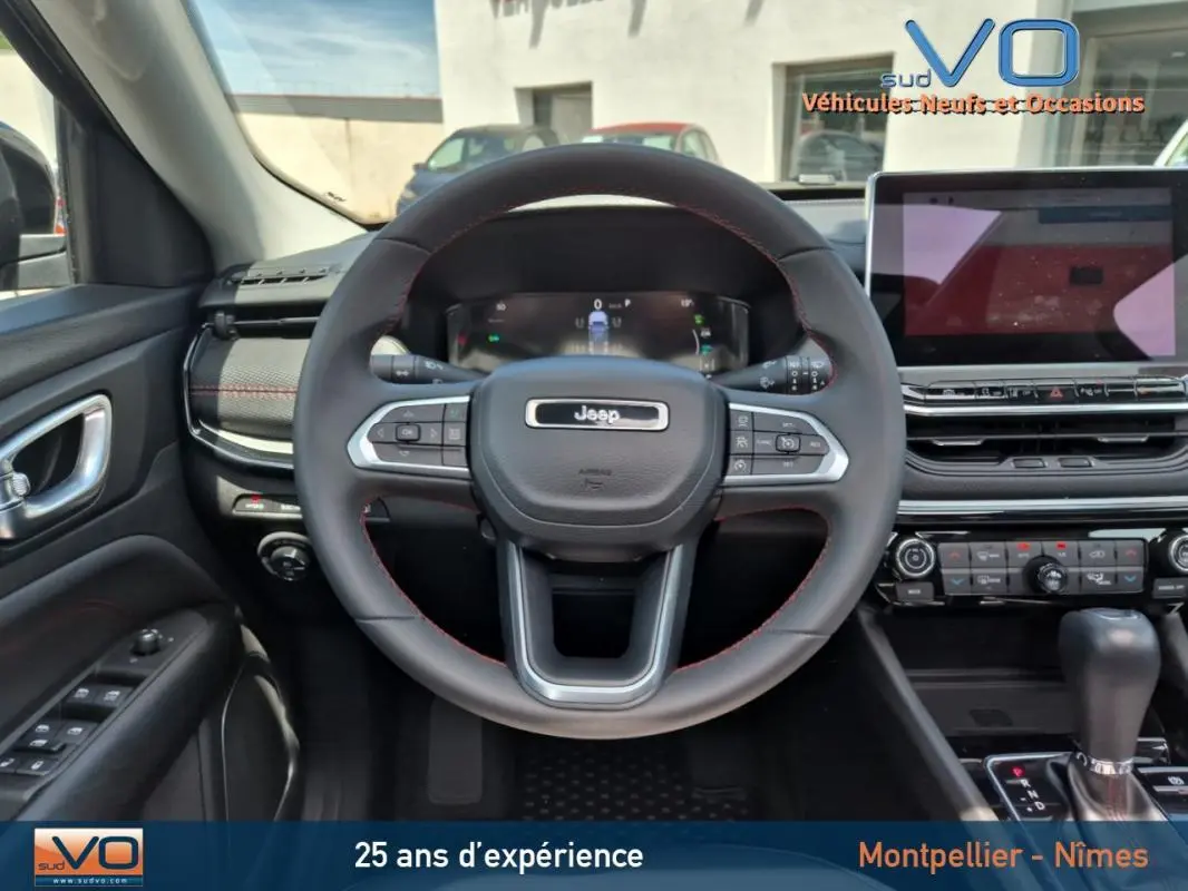 Vue intérieure centrée sur le volant du Jeep Compass gris foncé 2022 avec tableau de bord numérique et écran tactile.