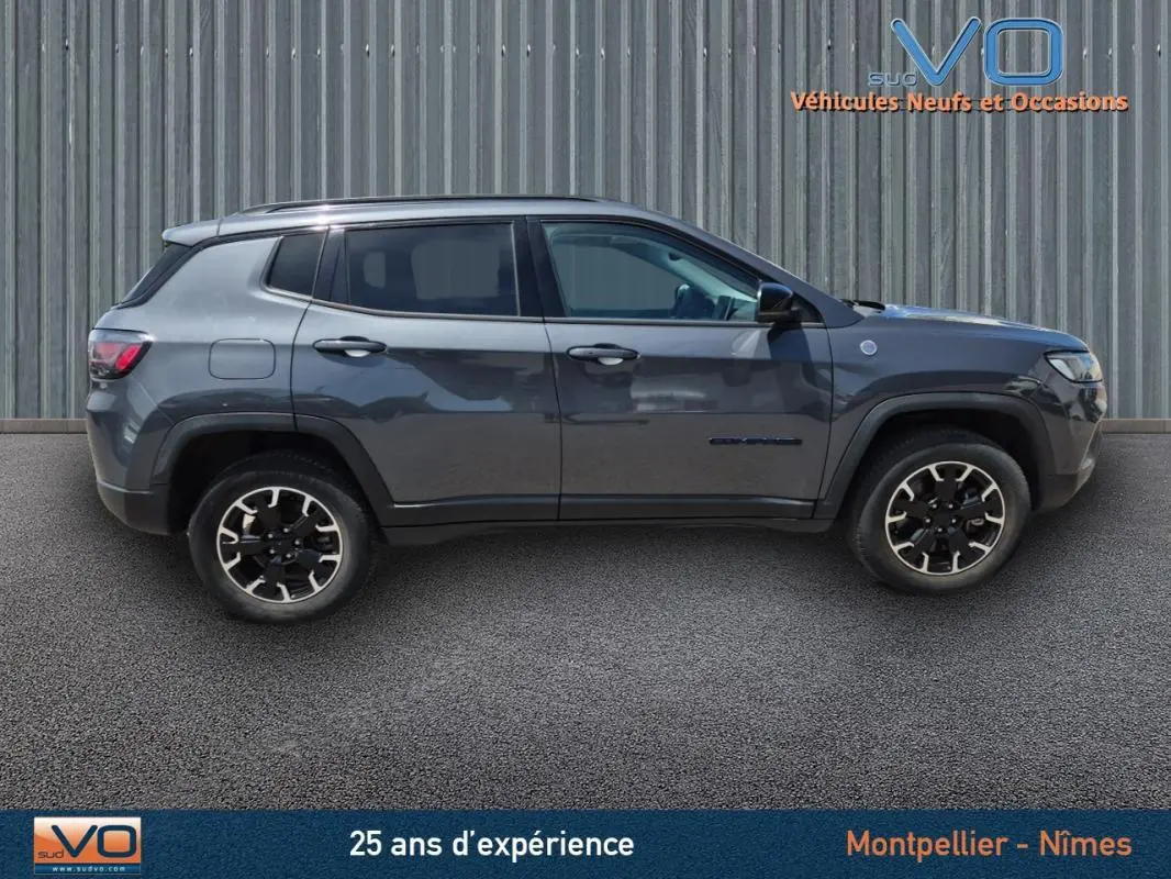 Profil côté gauche du Jeep Compass gris foncé 2022 Trailhawk hybride essence, mettant en valeur ses jantes distinctives.