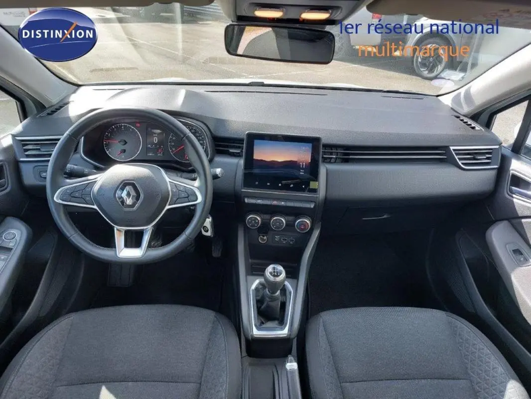 Vue intérieure avant de la Renault Clio blanche 2021, tableau de bord avec écran tactile et boîte manuelle visible.