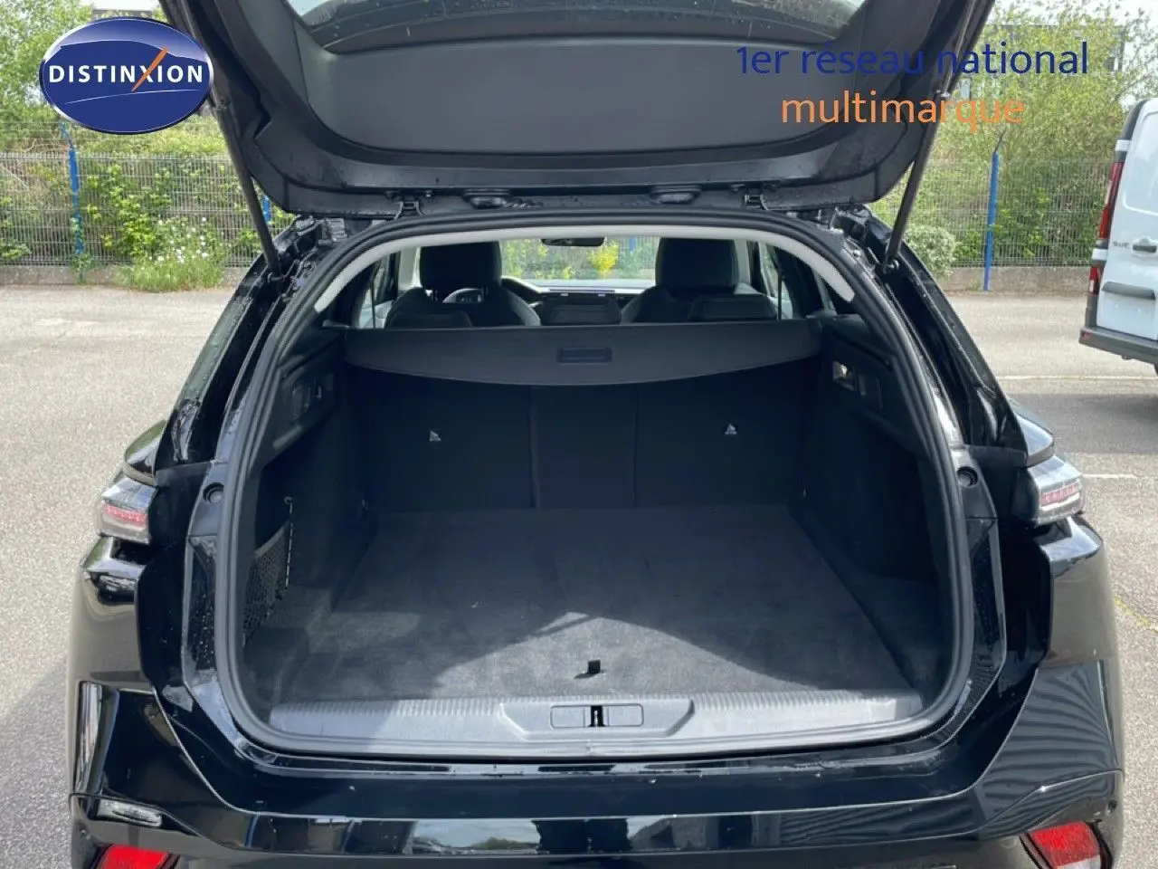 Vue arrière ouverte du coffre spacieux d'une Peugeot 308 SW Hybrid 145ch noire métal, avec hayon relevé en extérieur.