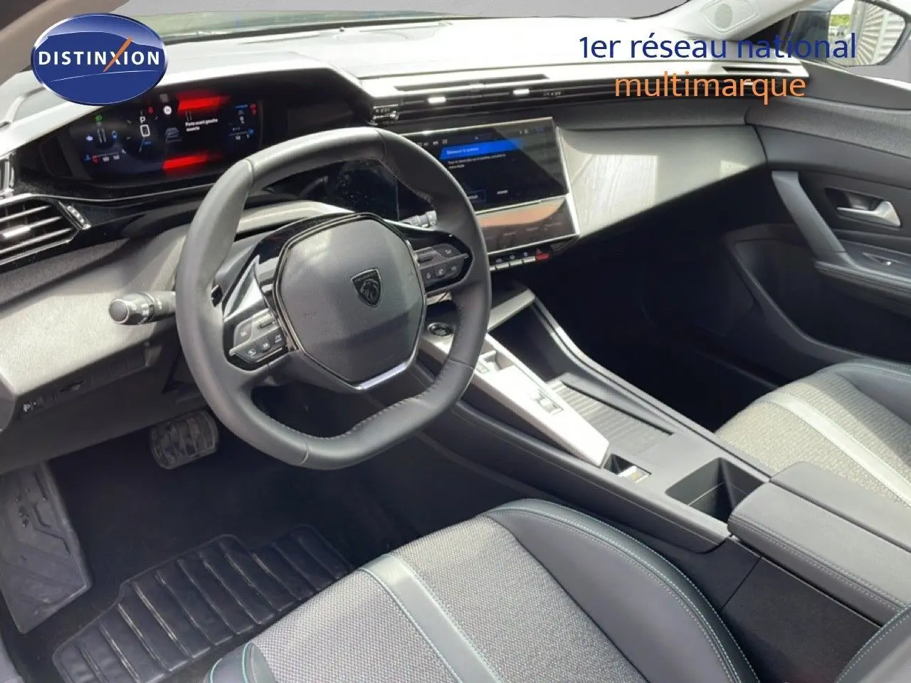 Vue intérieure du poste de conduite de la Peugeot 308 SW Hybrid 2025, avec volant cuir noir et écran tactile central.