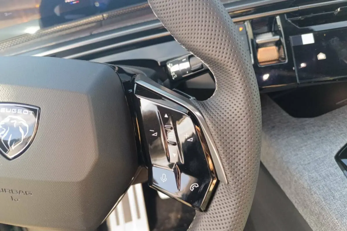 Gros plan sur le volant cuir perforé du Peugeot 3008 Hybrid 2025, avec commandes multifonctions et tableau de bord noir.