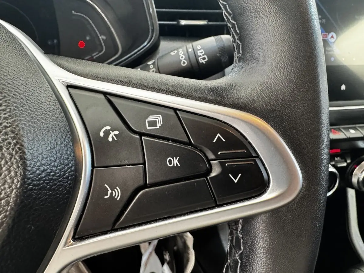 Gros plan sur les commandes multifonctions du volant cuir noir de la Renault Clio Business E-TECH 140 gris clair.