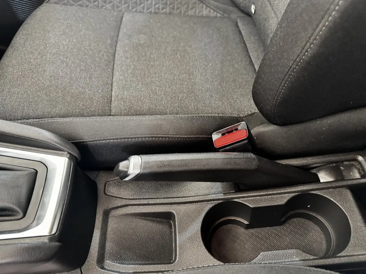 Gros plan sur la console centrale noire de la Renault Clio Business E-TECH 140, montrant frein à main et porte-gobelets.