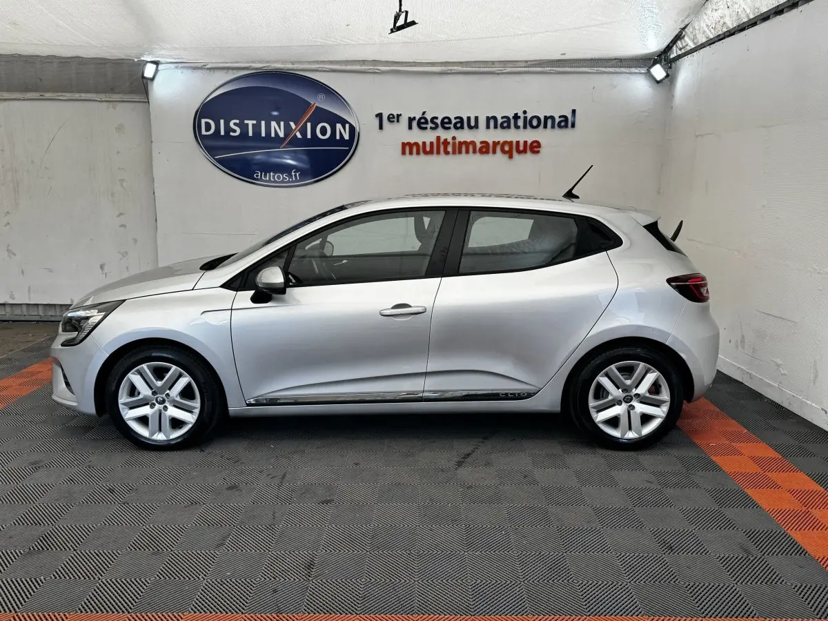 Vue de profil côté gauche d'une Renault Clio Business E-TECH 140 gris clair dans un showroom.