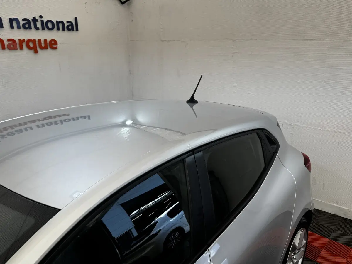 Vue 3/4 arrière droite d'une Renault Clio Business E-TECH 140 gris clair en intérieur avec toit et antenne visibles.