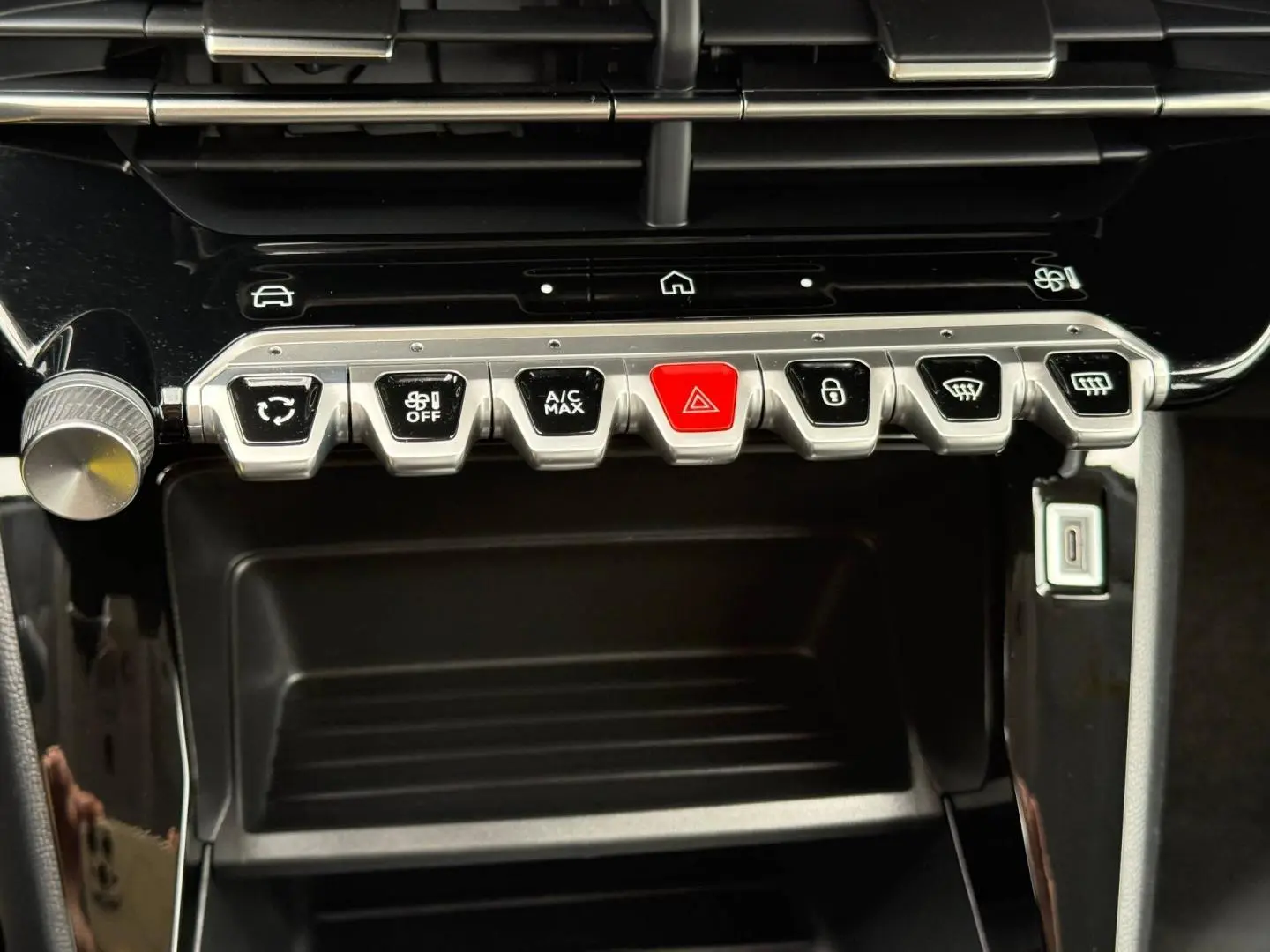 Vue rapprochée de la console centrale noire du Peugeot 208 1.2 Hybrid, avec boutons argentés et bouton rouge d’alerte.