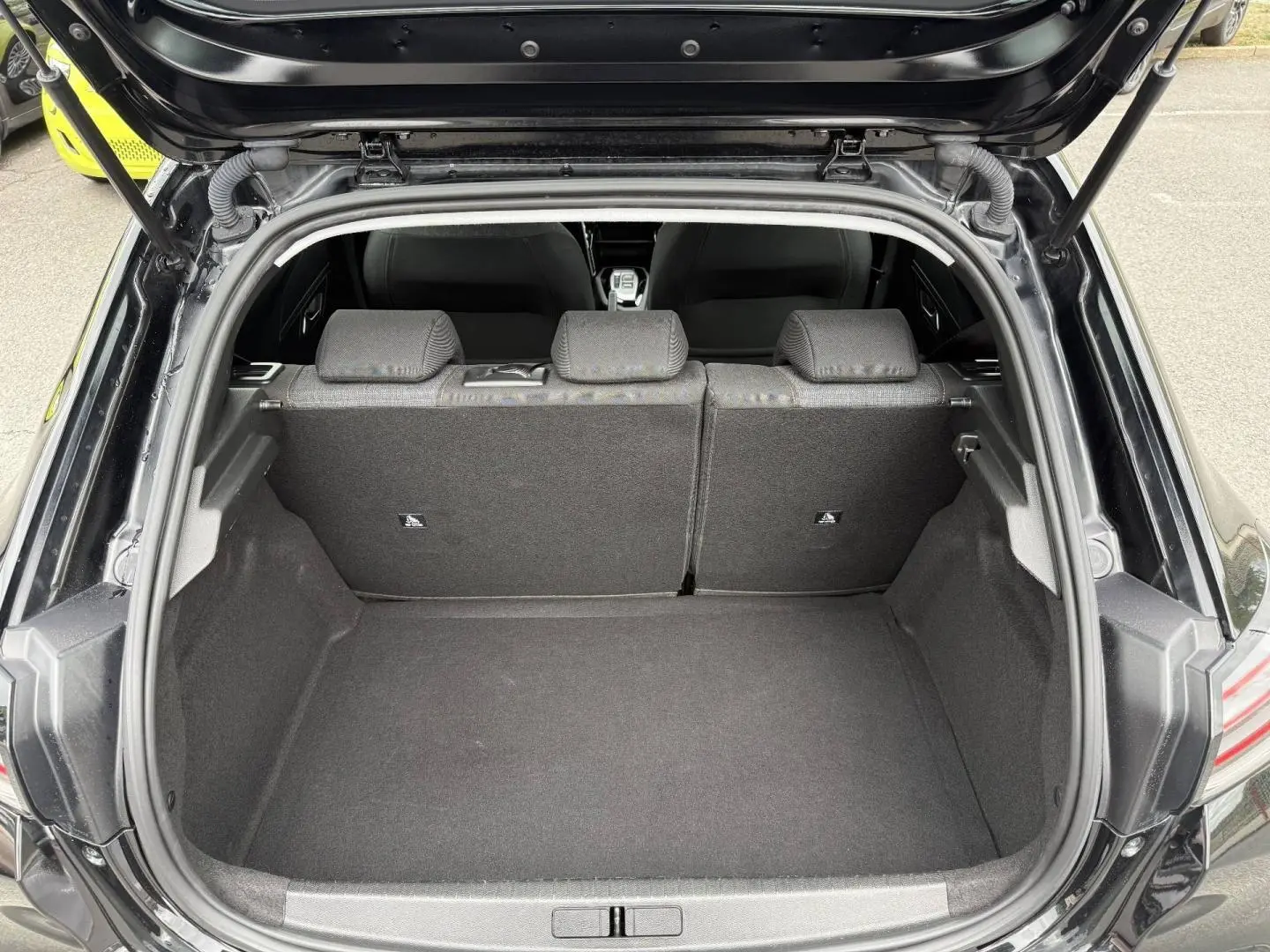 Coffre ouvert vu de l’arrière d’une Peugeot 208 noire Perla Nera avec banquette arrière en tissu gris.