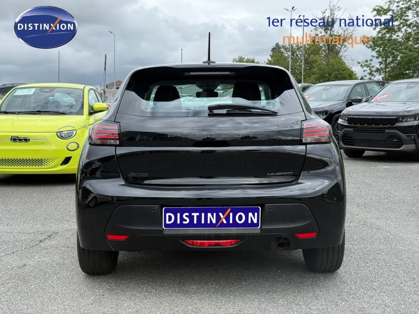 Vue arrière d'une Peugeot 208 noire Perla Nera, avec feux LED et logo distinctif sur un parking multimarques.