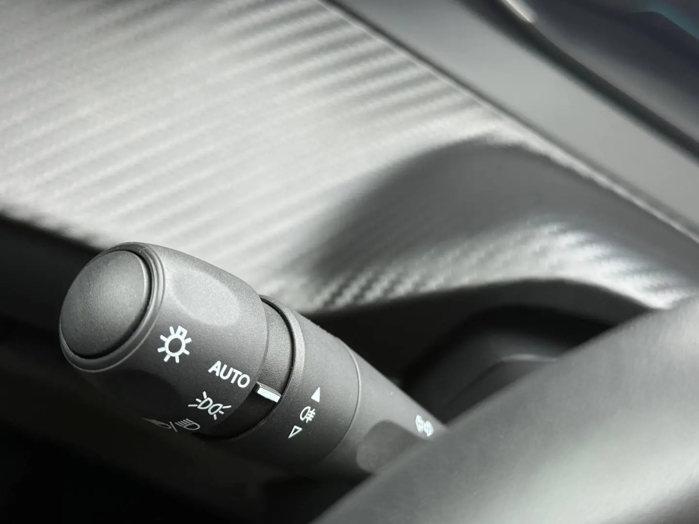 Gros plan sur la commande des phares automatique dans l'habitacle d'une Peugeot 208 noire Perla Nera.