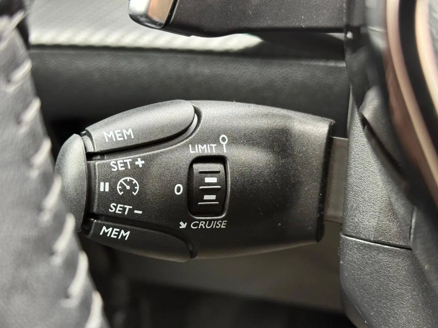 Gros plan sur la commande de régulateur de vitesse à gauche du volant dans l’habitacle noir du Peugeot 208 1.2 Hybrid 2025.