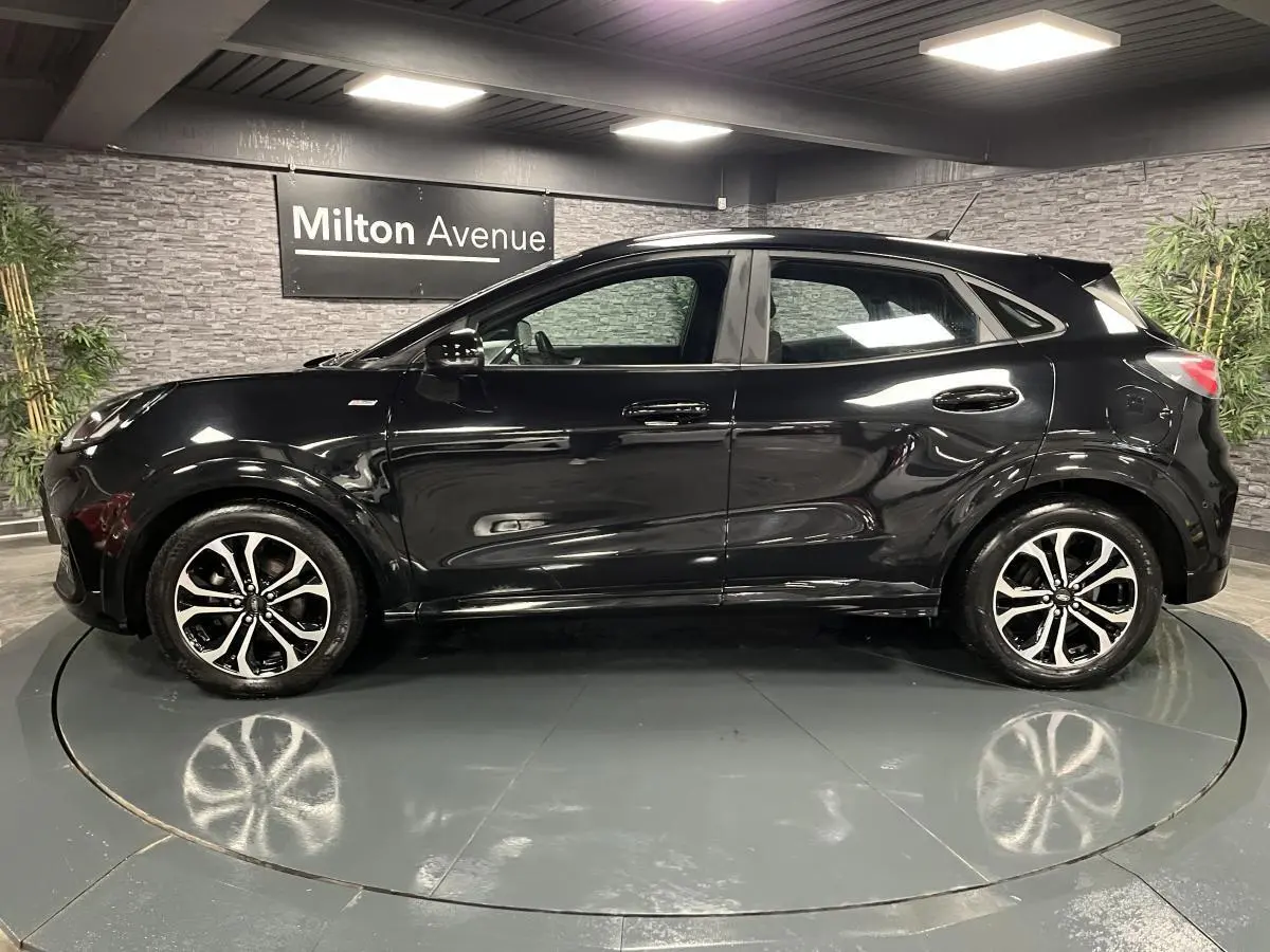 Ford Puma noir vue de profil côté gauche avec jantes alliage bicolores et toit noir brillant en intérieur showroom
