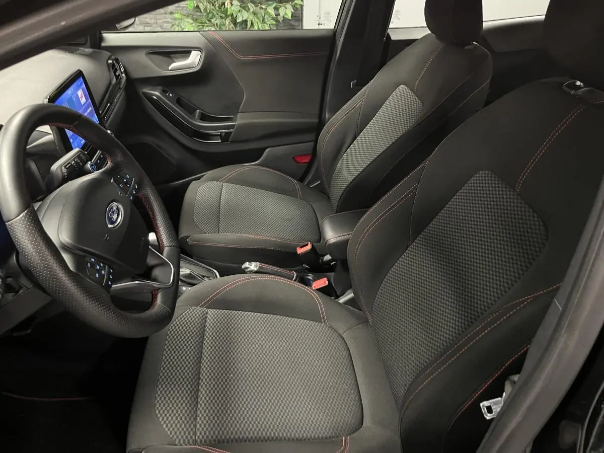 Vue intérieure côté conducteur du Ford Puma noir 2023, sièges tissu noir avec surpiqûres rouges et volant ST-Line.