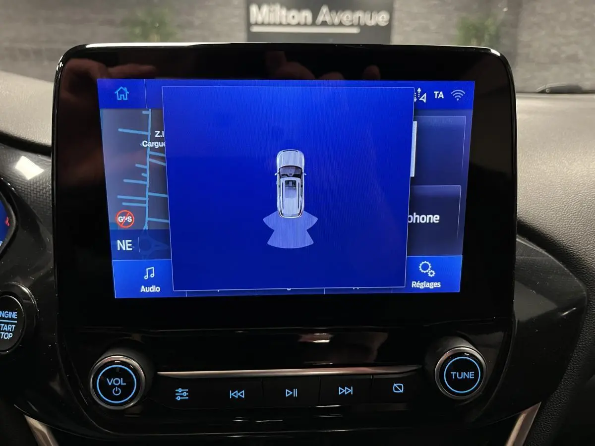 Écran tactile central du Ford Puma 2023 affichant l'aide au stationnement avec interface bleue et commandes audio.