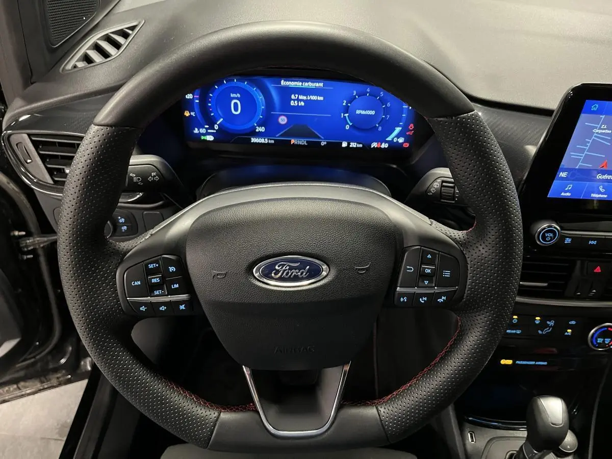Vue rapprochée du volant noir perforé avec surpiqûres rouges et tableau de bord numérique bleu du Ford Puma 2023.