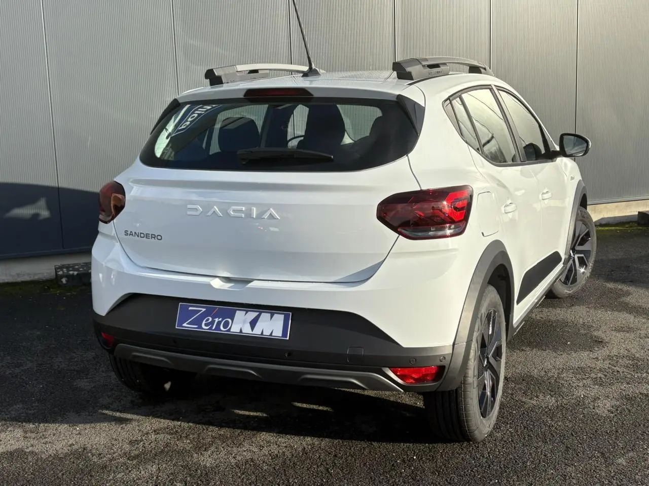 Vue 3/4 arrière droite du Dacia Sandero Stepway blanc glacier avec barres de toit et jantes noires.