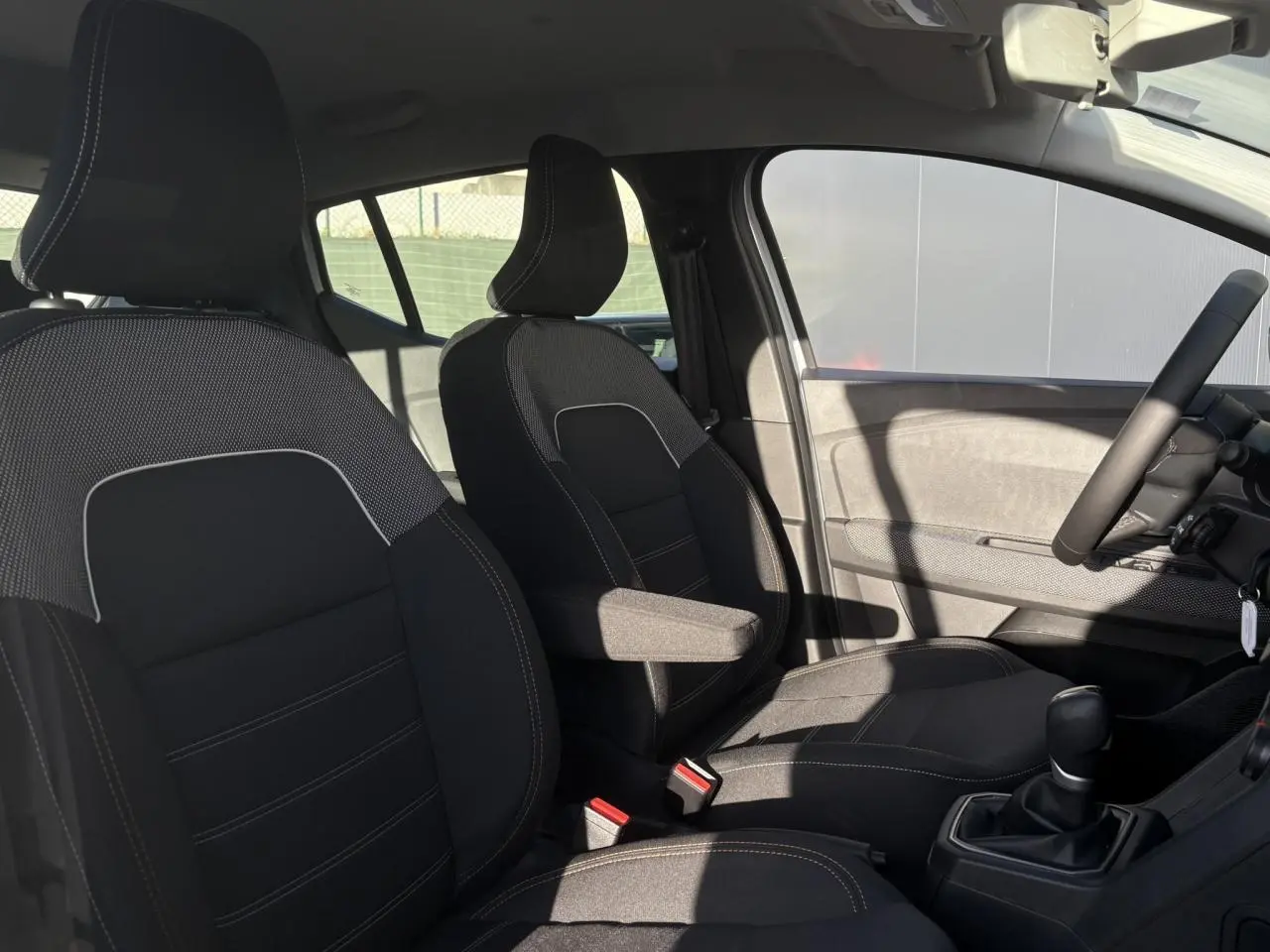 Intérieur de la DACIA Sandero Stepway 2024, vue côté droit sur sièges noirs avec accoudoir conducteur et volant.