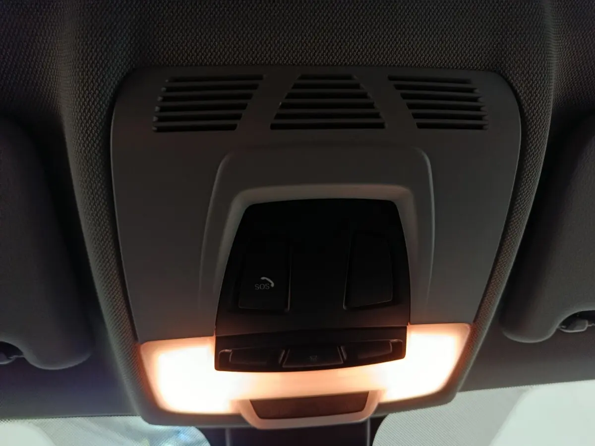 Vue intérieure en gros plan du plafonnier avec boutons SOS et éclairage allumé dans un BMW X1 gris foncé 2021.