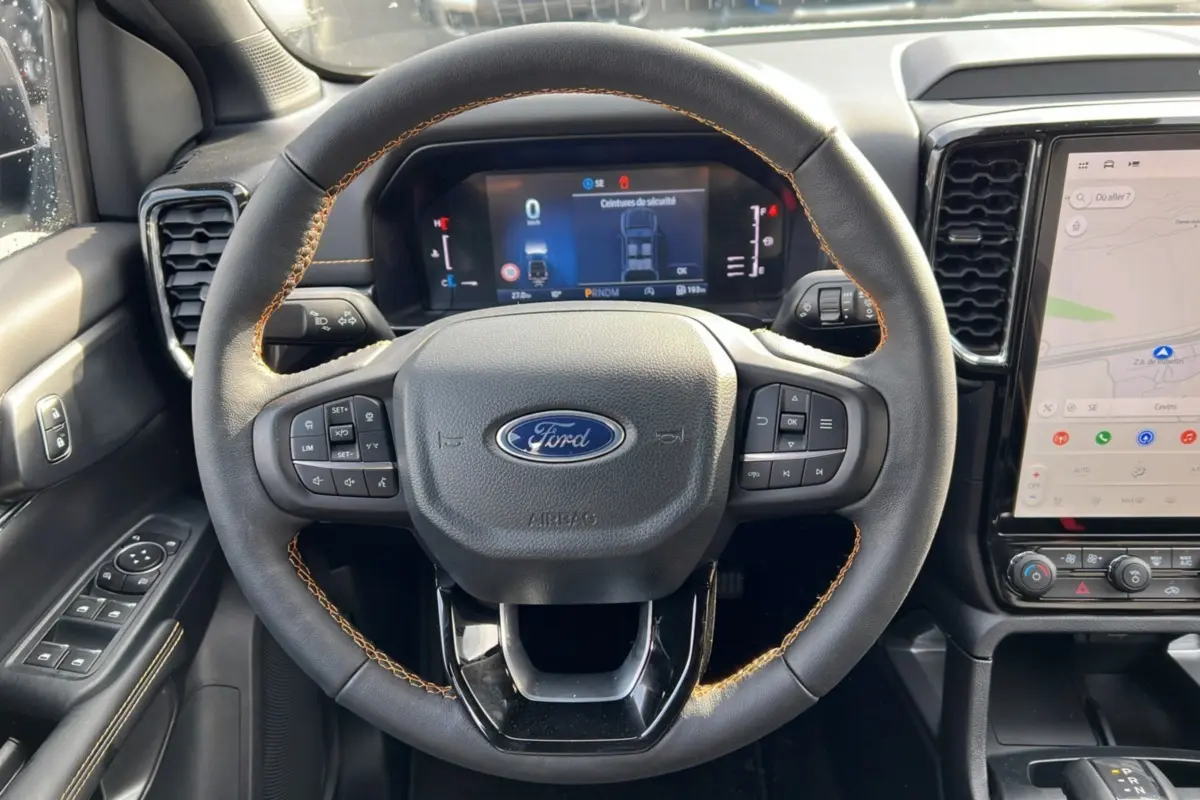 Vue intérieure centrée sur le volant cuir noir avec surpiqûres marron du Ford Ranger 2025, tableau de bord numérique et écran tactile.