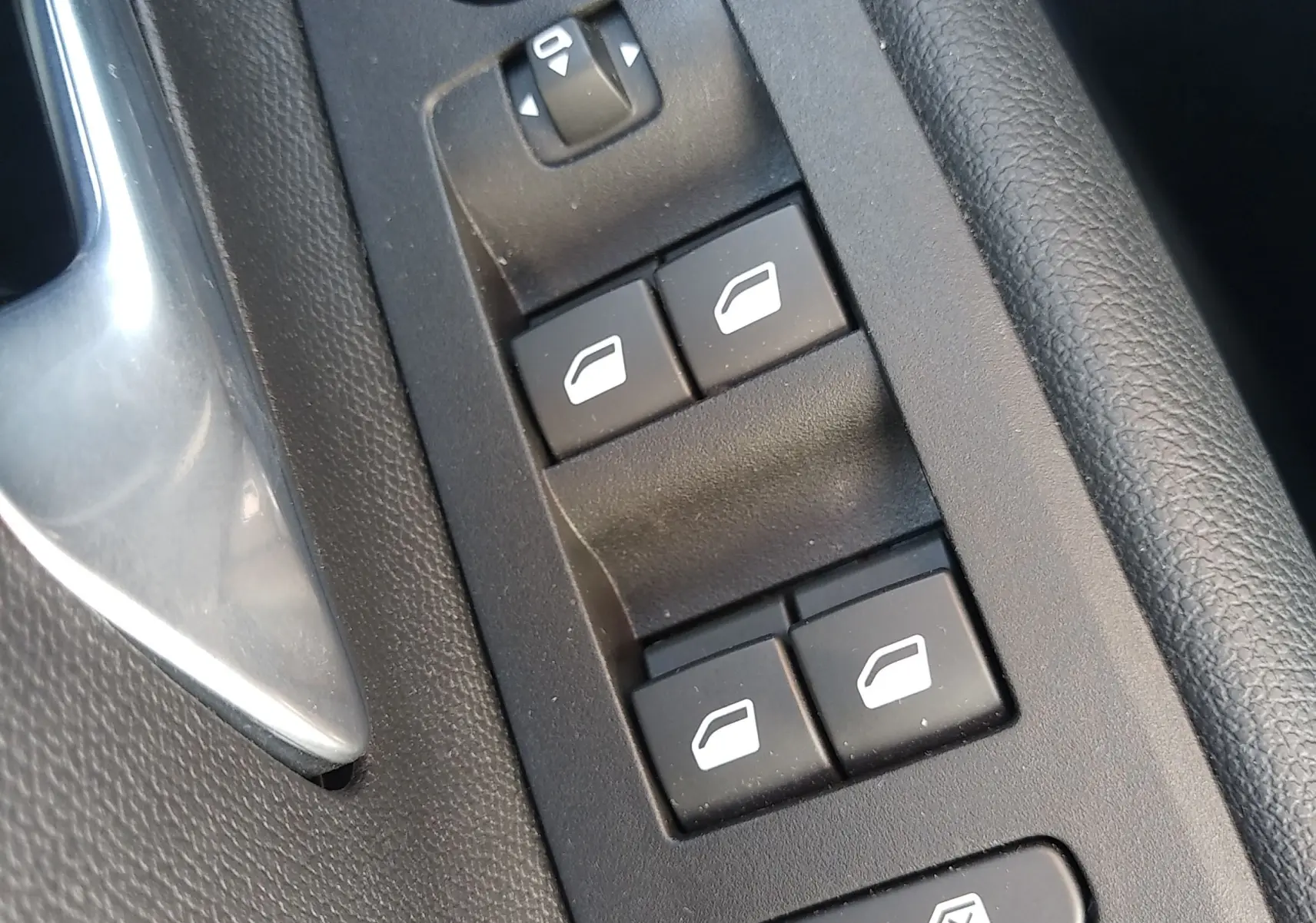 Gros plan sur les commandes de lève-vitres et réglage des rétroviseurs côté conducteur de l'Opel Mokka Electric gris 2025.