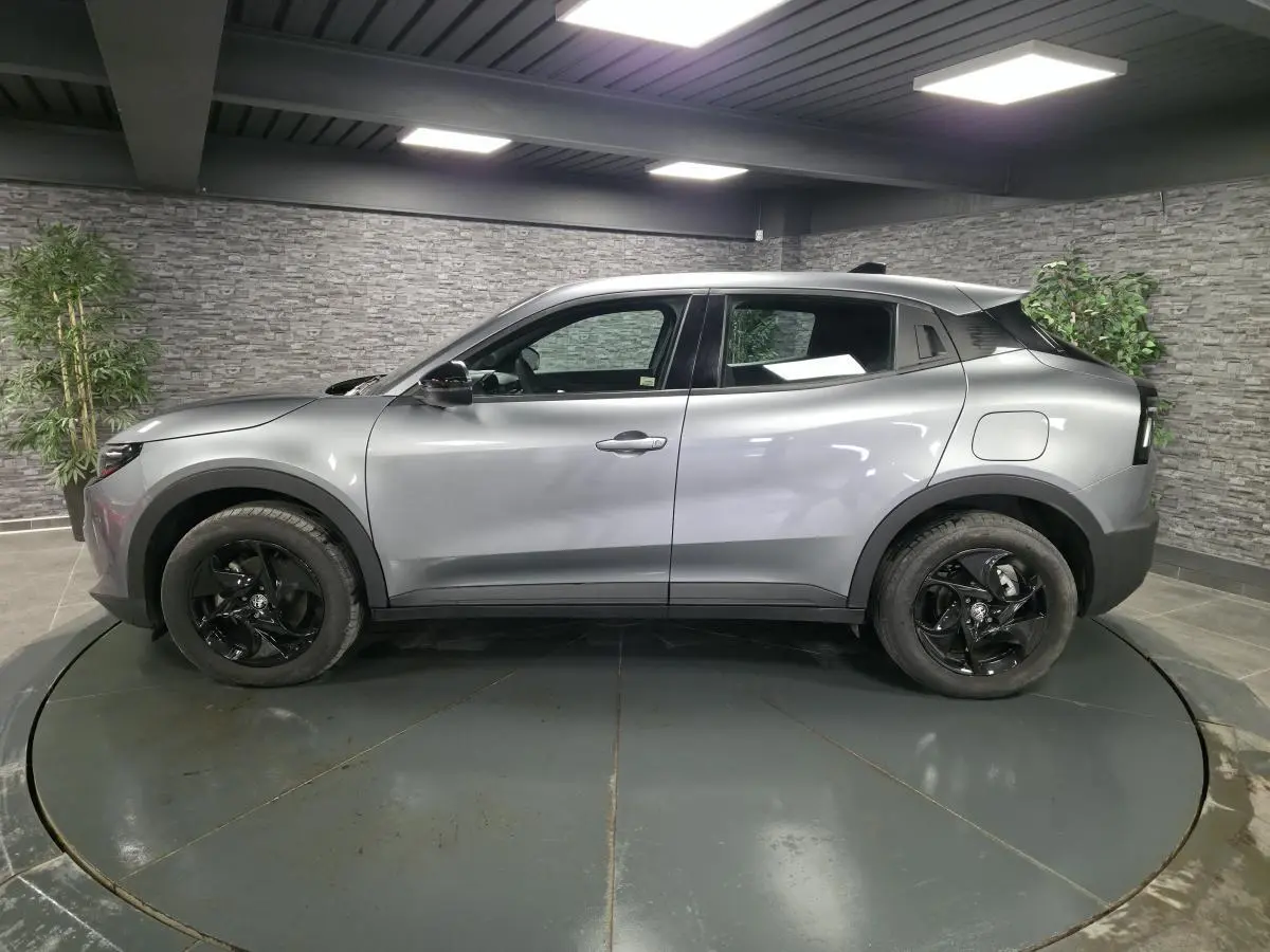Vue de profil côté gauche d'une Alfa Romeo Junior 1.2 Ibrida grise avec jantes alliage noires dans un showroom.