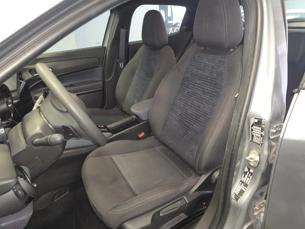 Vue intérieure côté conducteur de l'Alfa Romeo Junior 1.2 Ibrida 2025 gris, sièges tissu Icona et accoudoir central.