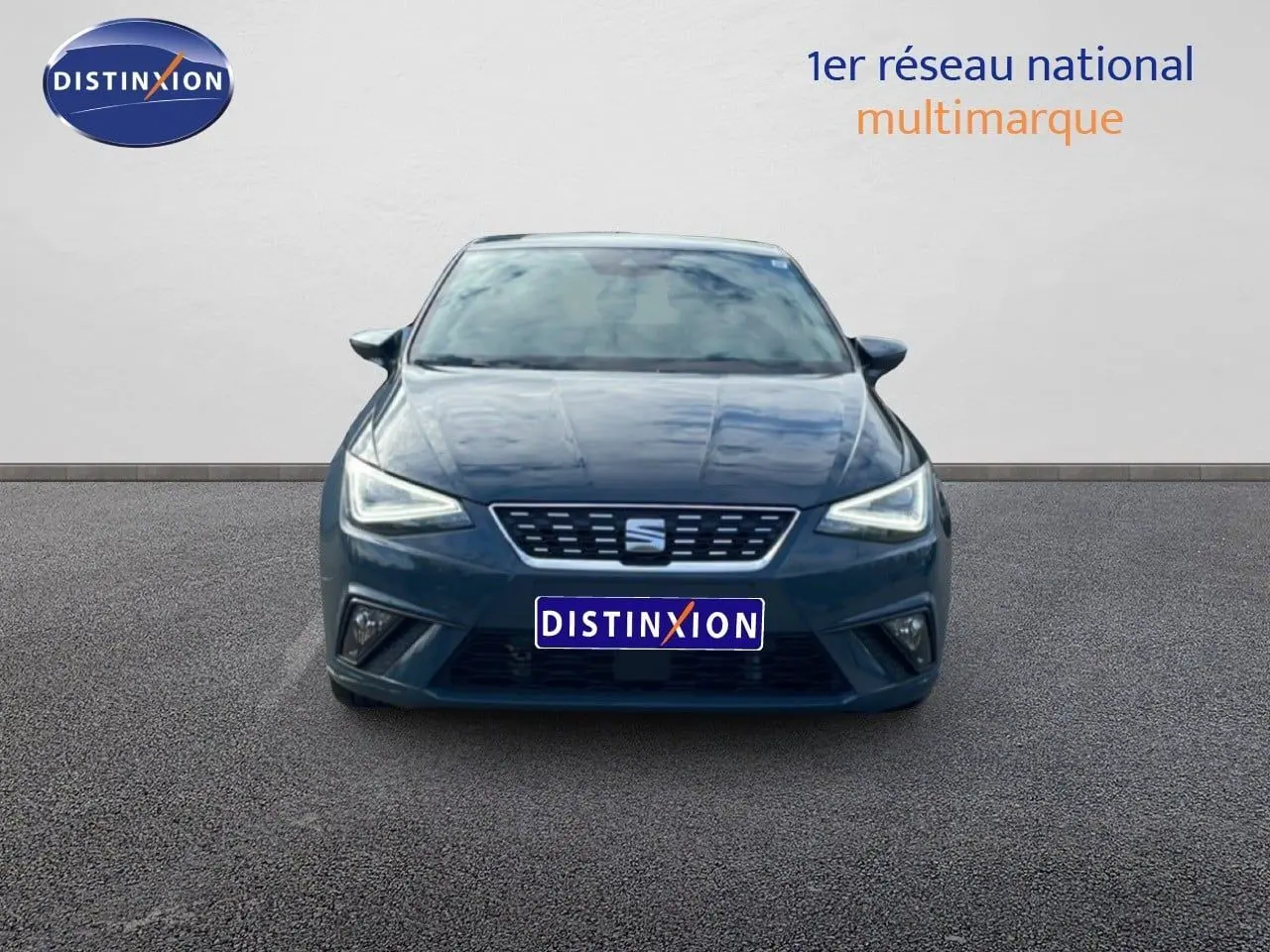 Vue frontale d'une SEAT Ibiza bleu fjord 2025 avec phares LED allumés sur un sol goudronné.