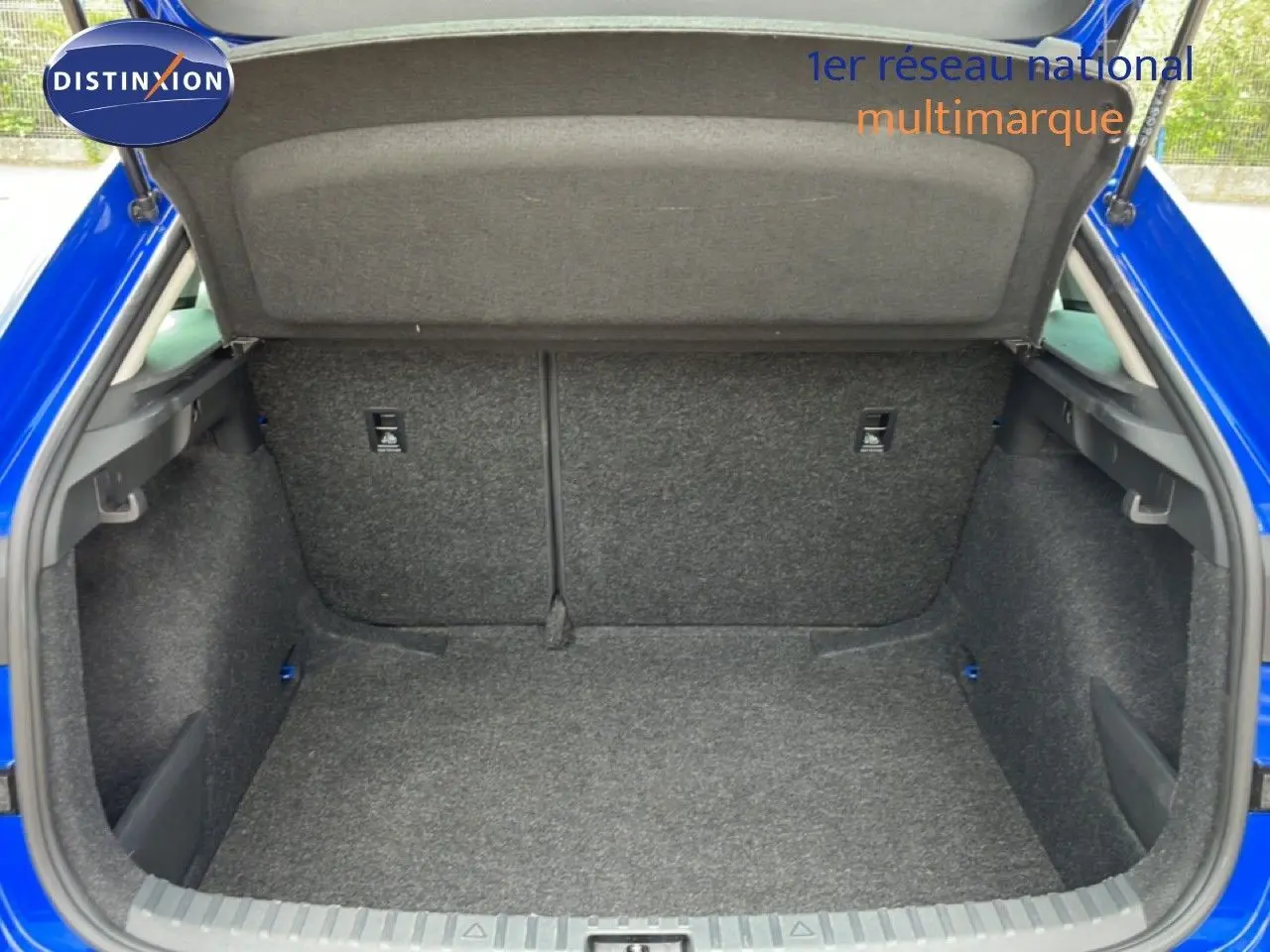 Coffre ouvert vu de l'arrière d'une Skoda Scala bleu racing metal, montrant l'espace de chargement vide et la moquette grise.