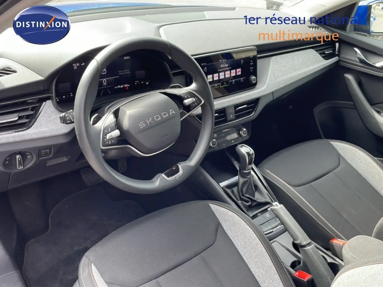 Vue intérieure côté conducteur de la Skoda Scala 2025, volant multifonction, sellerie tissu gris et noir, console centrale avec boîte auto.