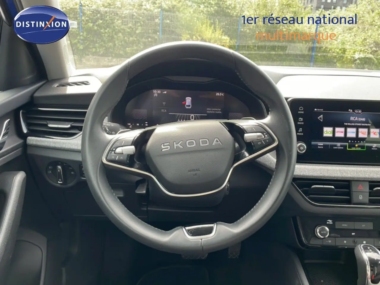 Vue intérieure centrée sur le volant SKODA d'une Scala 2025, avec tableau de bord numérique et écran tactile visible.