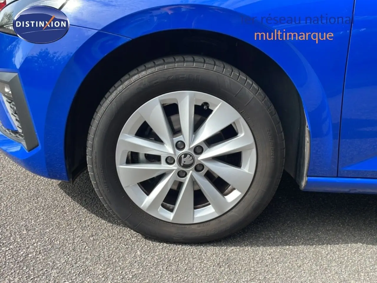 Gros plan sur la roue avant gauche d'une Skoda Scala bleu racing metal avec jante argentée et logo central visible.