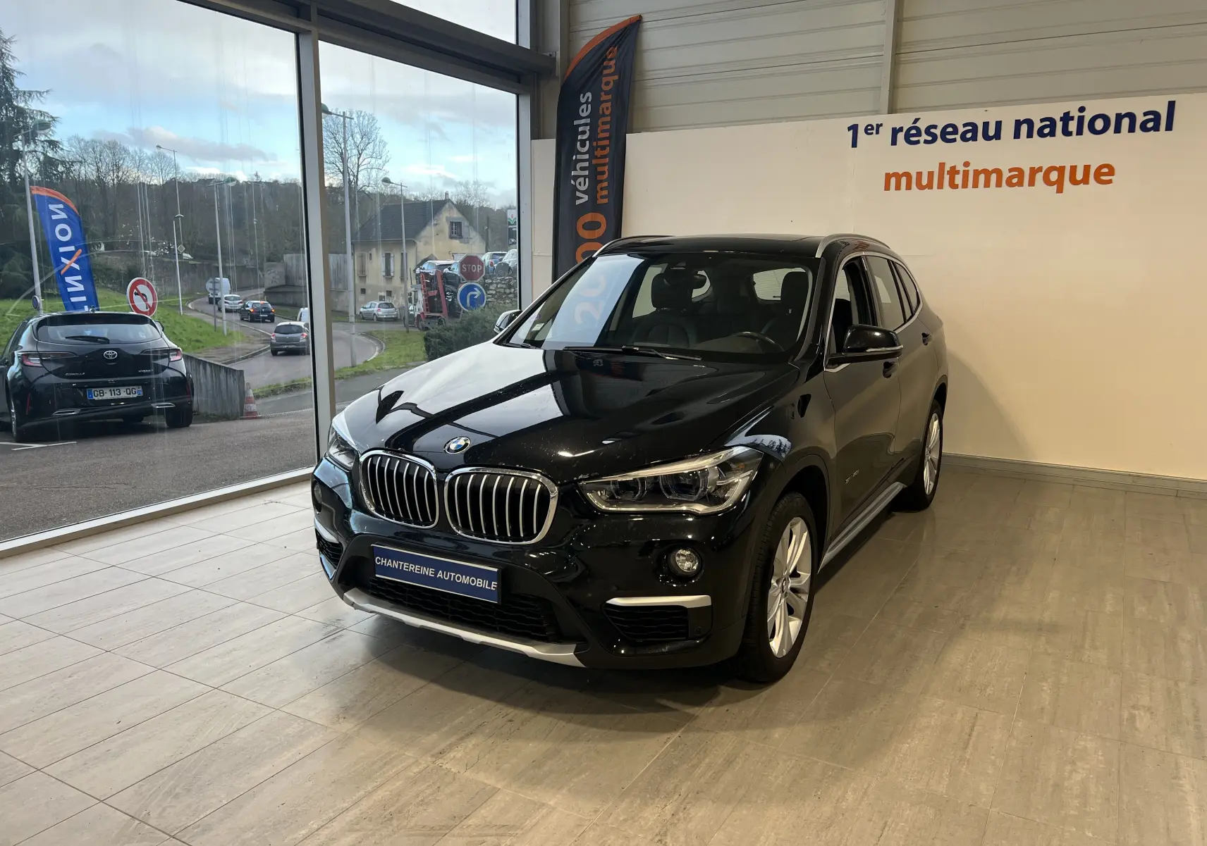 BMW X1 F48 Saphirschwarz en 3/4 avant droit, SUV compact diesel exposé en showroom lumineux.