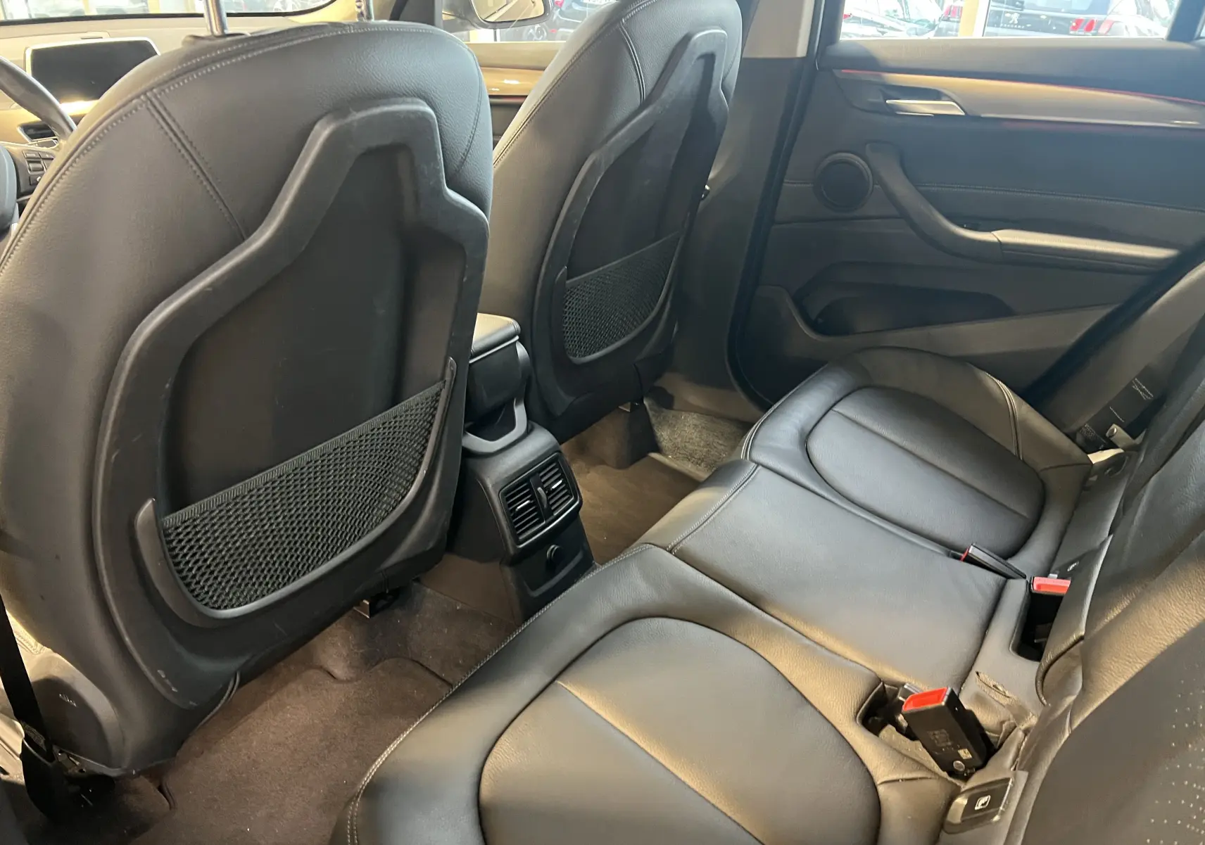 Vue intérieure arrière du BMW X1 F48 noir, montrant les sièges en cuir et les aérateurs centraux entre les sièges avant.