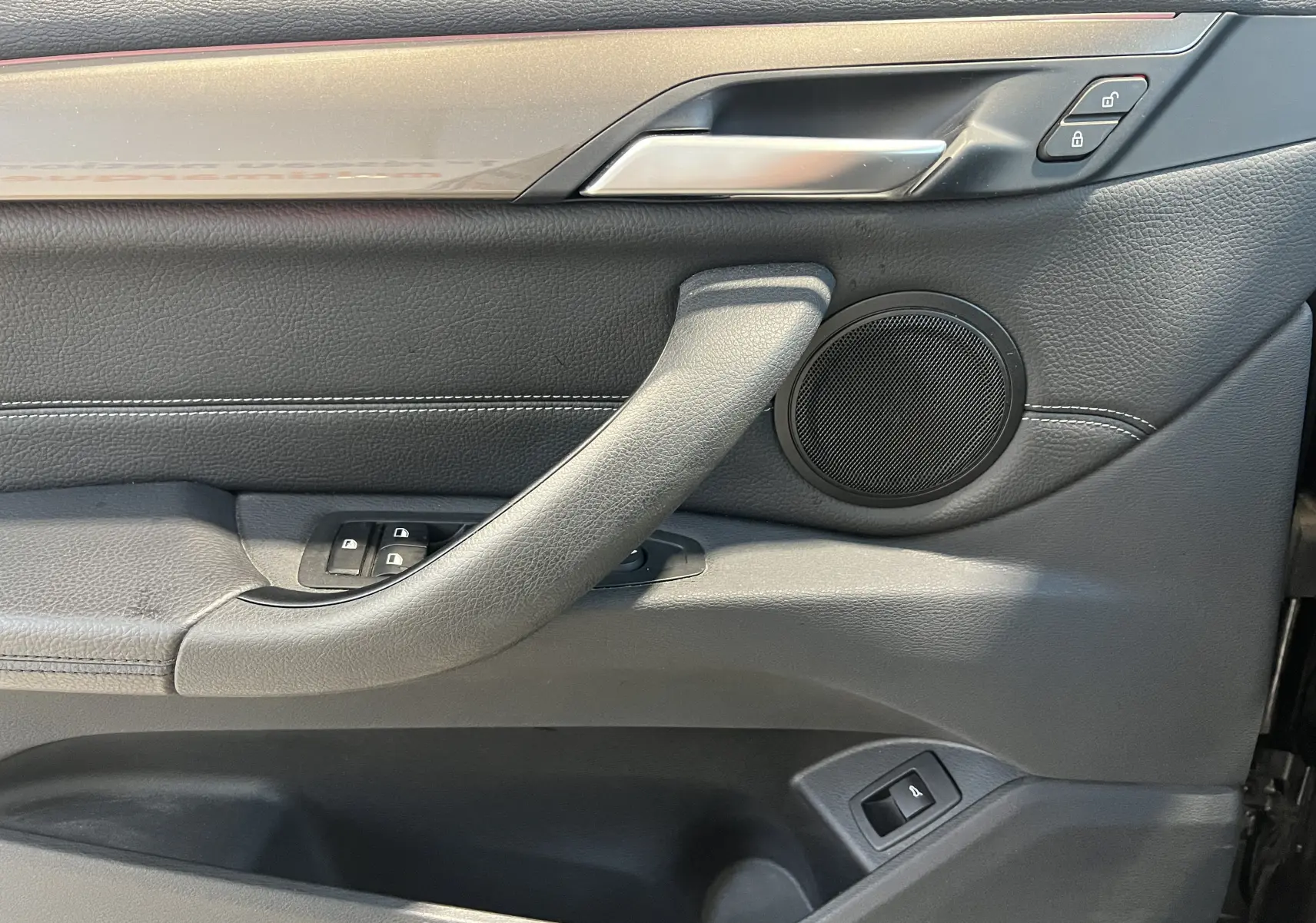 Détail de la porte avant gauche intérieure de BMW X1 F48 noire, avec commandes de vitres et haut-parleur rond.
