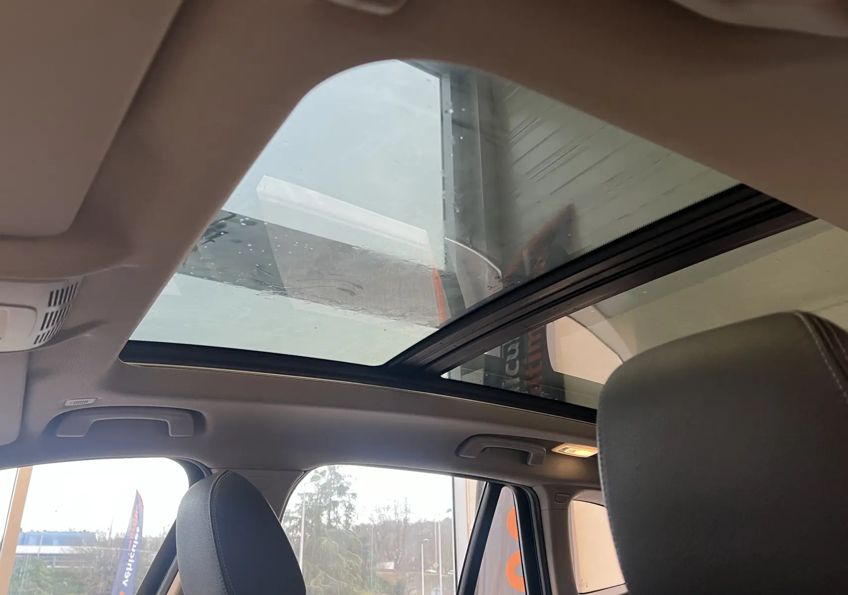 Toit panoramique ouvert visible depuis l'intérieur du BMW X1 F48 noir, avec sièges avant en cuir gris.