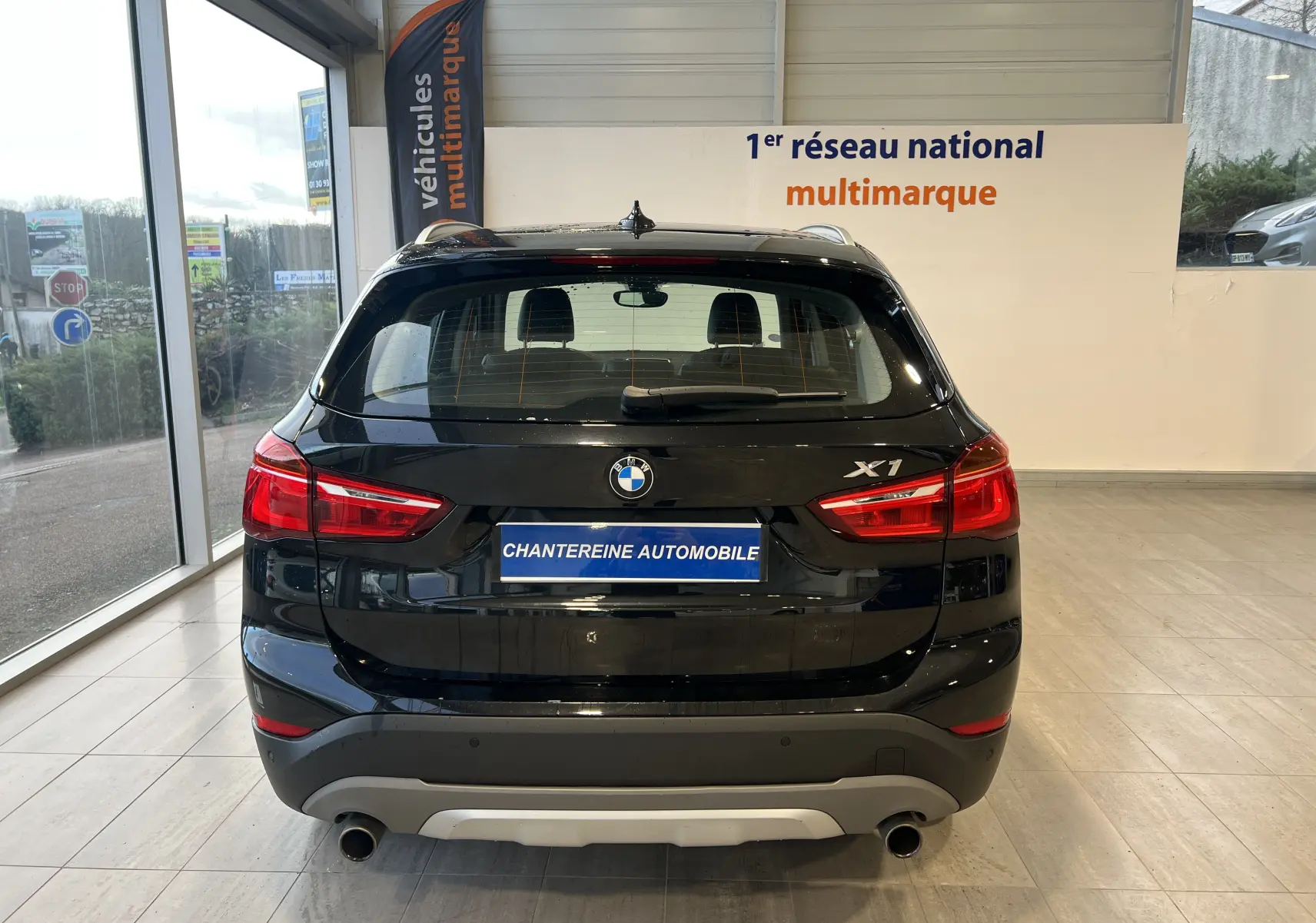 Vue arrière d'un BMW X1 F48 noir Saphirschwarz 2017, avec logo et feux rouges distinctifs en intérieur showroom.
