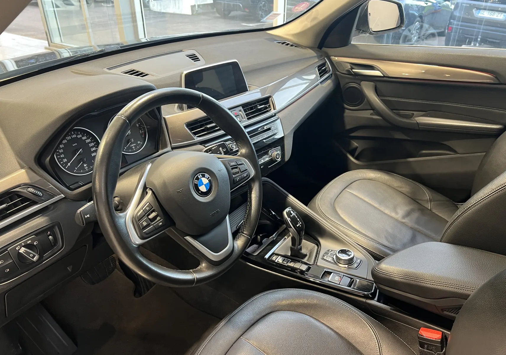 Intérieur du BMW X1 F48 noir, vue côté conducteur, tableau de bord moderne avec volant multifonction et console centrale.