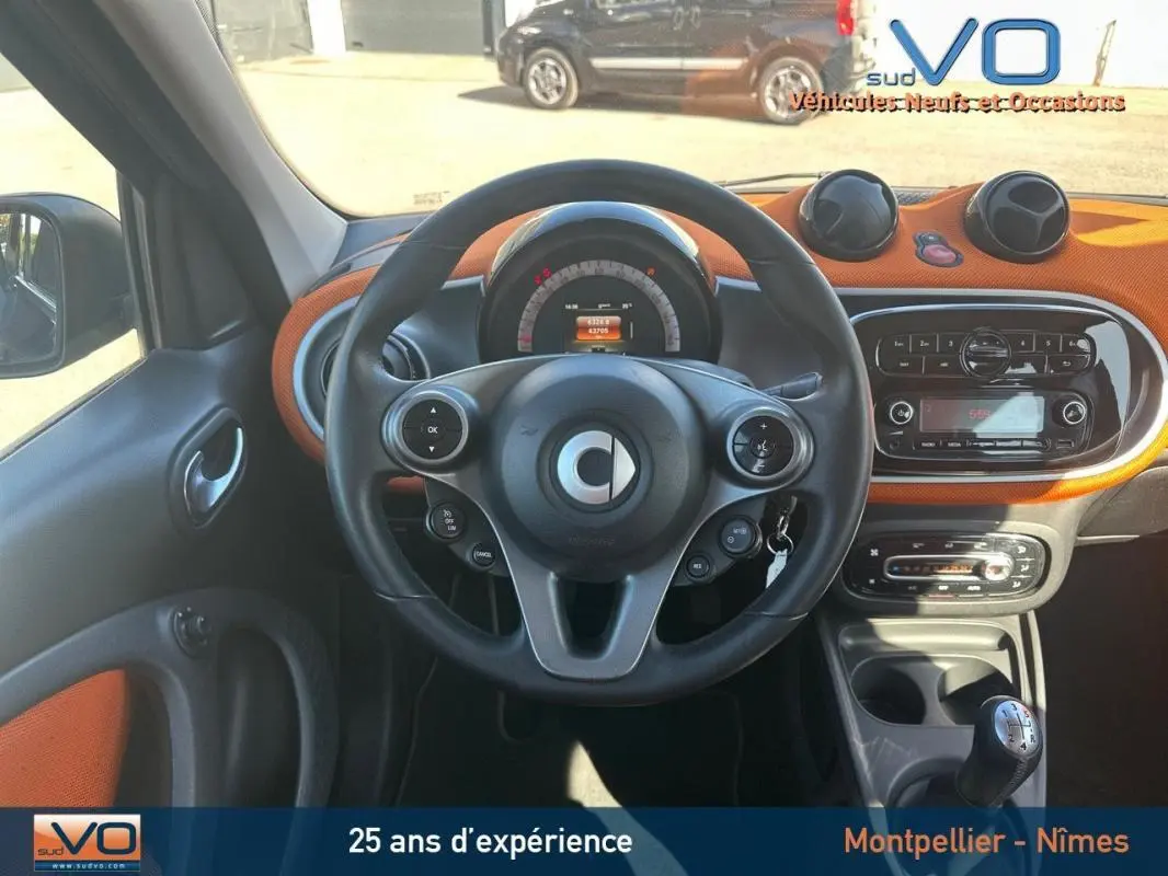 Vue intérieure centrée sur le volant multifonctions et tableau de bord orange d'une Smart Forfour noire de 2015.