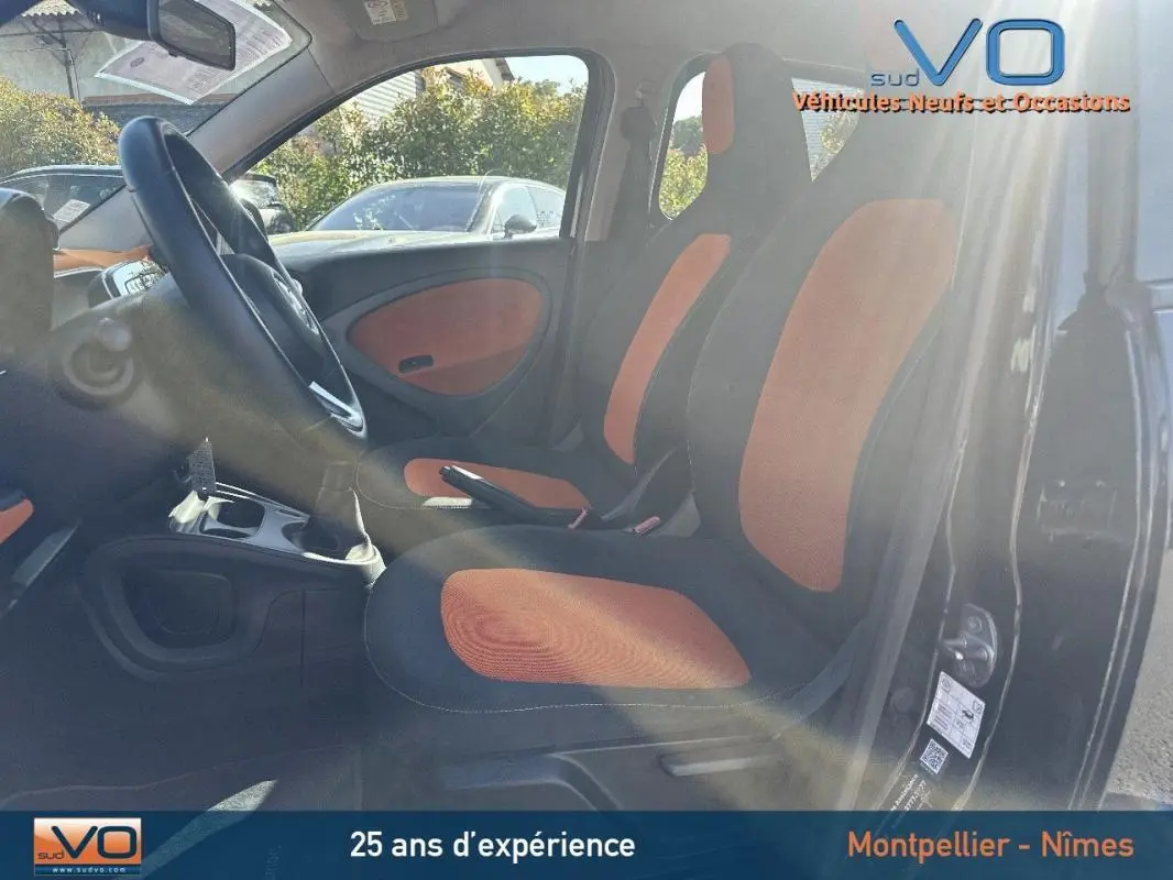 Intérieur de la Smart Forfour noir, vue côté gauche montrant les sièges bi-color orange et noir et le volant multifonctions.