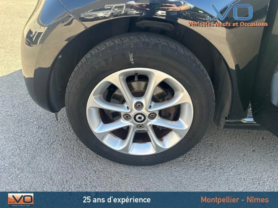 Gros plan sur la roue avant droite d'une Smart Forfour noire de 2015, mettant en valeur la jante en alliage et le logo central.