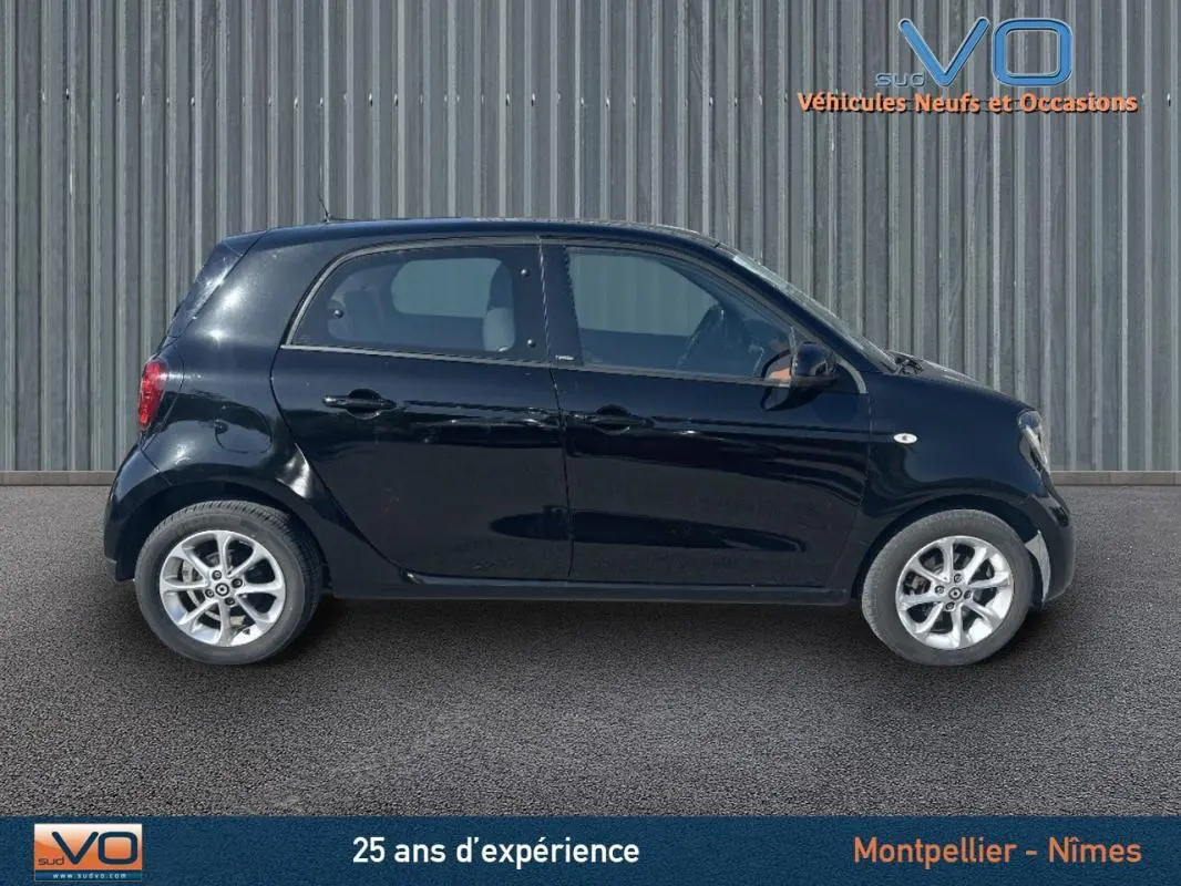 Vue latérale droite d'une Smart Forfour noire de 2015, compacte et élégante sur fond industriel.