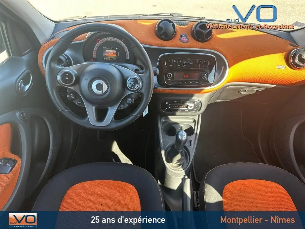 Vue intérieure avant de la Smart Forfour noire 2015, tableau de bord orange avec volant multifonctions et boîte manuelle.