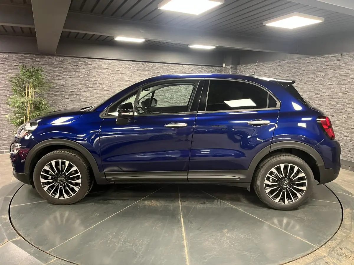Profil côté gauche d'un Fiat 500X bleu métallisé 2024 avec jantes alliage 17 pouces et vitres surteintées.
