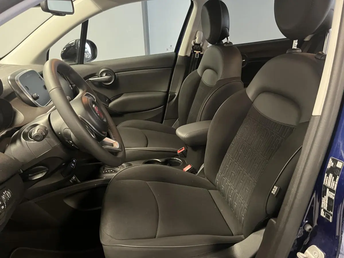 Intérieur avant de la Fiat 500X 2024 bleu, sièges noirs avec monogramme FIAT et accoudoir central visible.