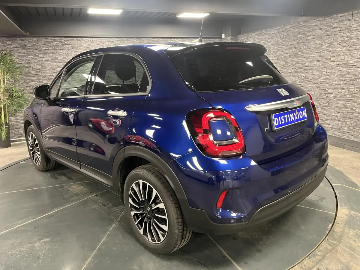 Vue 3/4 arrière droite d'une Fiat 500X 2024 bleu métallisé avec jantes alliage 17'' et vitres surteintées.