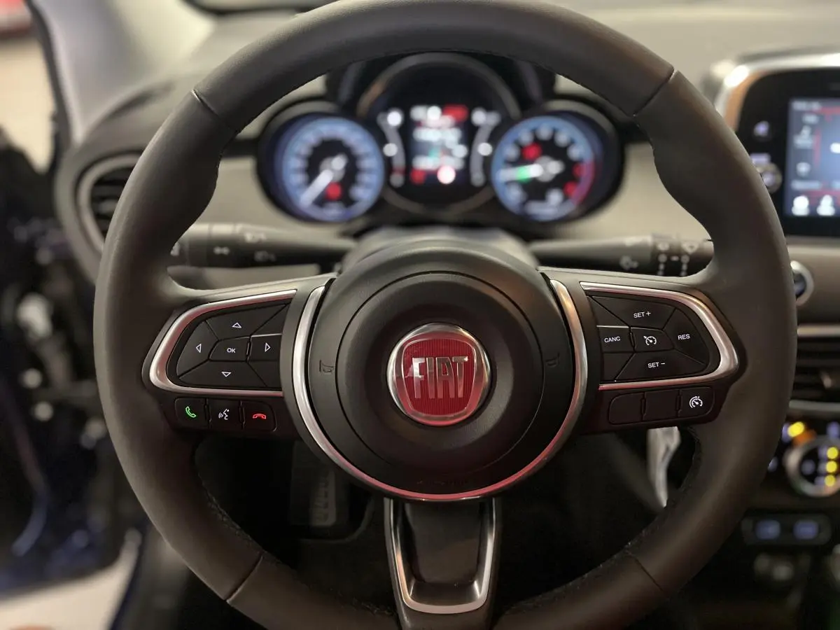 Volant Fiat 500X 2024 en cuir avec commandes intégrées, tableau de bord numérique flou en arrière-plan.